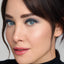 Close-up of a person with dark hair and blue eyeshadow against a neutral background