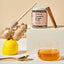Jar of Turmeric Ginger Tonic with ingredients like ginger root, lemon, and cinnamon on a beige background