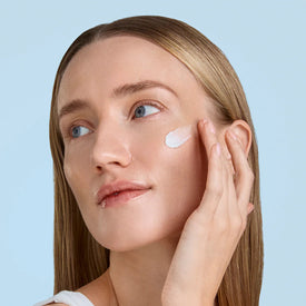 Woman applying cream to her face against a light blue background